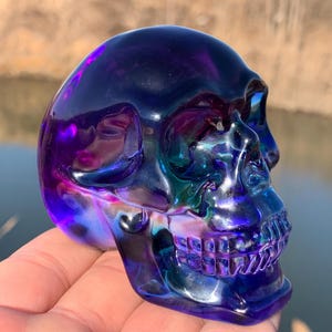 May include: A purple and blue iridescent glass skull with a detailed face and teeth.