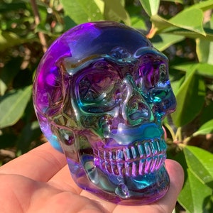 May include: A crystal skull sculpture with iridescent purple, blue, and green colors. The skull is detailed with a realistic face and teeth.