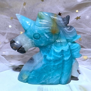 May include: A carved stone unicorn head sculpture in shades of blue, white, and gray. The unicorn has a pointed horn, a flowing mane, and a detailed face. The sculpture is approximately 6 inches tall.