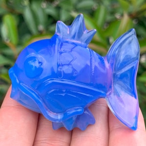 May include: A blue glass fish figurine with a iridescent finish. The fish has a crown on its head and a detailed body.