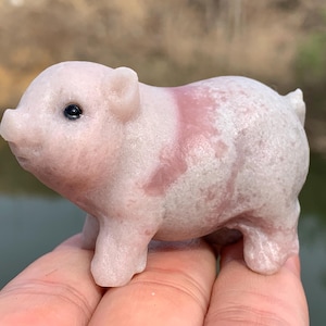 以下が含まれることがあります： ピンクと白のマーブル模様が施された、小さな白いブタの置物。置物は磨かれた石で作られており、滑らかで光沢のある仕上がりです。