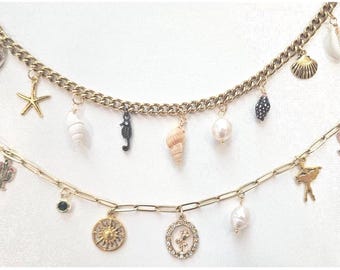 May include: Two gold-toned necklaces with various charms. The top necklace has a curb chain with seashell, starfish, and seahorse charms. The bottom necklace has a paperclip chain with a sun, flower, and pearl charms. The charms are in various colors.