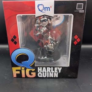 May include: A Harley Quinn Q-Fig figurine in a display box. The figurine is in a dynamic pose, wearing a red and black costume with a jester hat. The box has the QMx and Loot Crate logos.