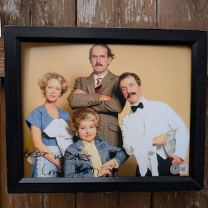 以下が含まれることがあります： 黒いフレームに入った4人の写真。写真には手書きの「Best Wishes」という文字とサインが含まれています。被写体は、ブレザー、ドレス、タキシードなど、さまざまな服装をしています。