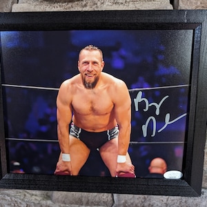 Könnte beinhalten: Gerahmtes Foto eines lächelnden Wrestlers in einem Wrestling-Ring. Der Wrestler trägt eine schwarz-weiße Hose und Handgelenkbänder. Das Foto ist signiert und in einem schwarzen Holzrahmen gerahmt.