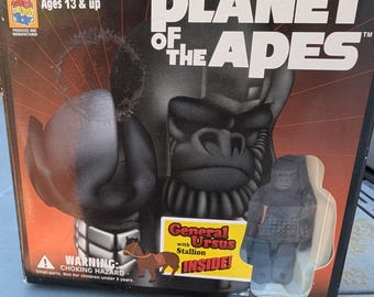 Könnte beinhalten: Eine schwarze Box mit einem weißen Bild eines Gorillas und dem Text "Planet der Affen" auf der Vorderseite. Die Box ist für ein Kubrick-Spielzeugset und es steht "Alter 13+ Jahre" und "General Ursus mit Hengst im Inneren!" auf der Vorderseite.