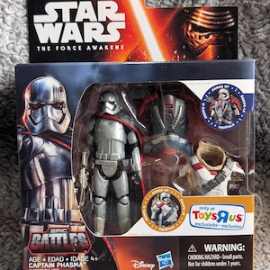 May include: A Star Wars Epic Battles Captain Phasma action figure in its original packaging. The figure is silver and black, with a blaster. The packaging includes the Star Wars logo and the text "The Force Awakens".