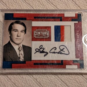 May include: A Panini Century Collection trading card featuring a portrait of a man in a suit and tie, with a signature and a patch with red, white, and blue stripes. The card is encased in a clear protective holder.