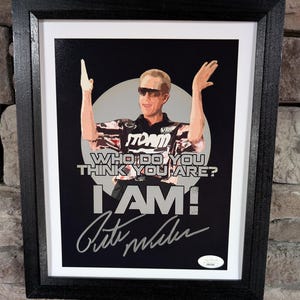 May include: A black and white image of a man wearing a black and red bowling shirt with the word "Storm" on it. He is holding his arms up in the air and smiling. The text "Who do you think you are? I AM!" is written in white letters on a black background. The man's signature is written in silver below the text.