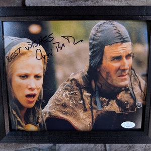 Puede incluir: Una fotografía en blanco y negro enmarcada de dos actores, una mujer con cabello rubio y un hombre con una prenda oscura con capucha. La mujer mira hacia la derecha y el hombre mira hacia adelante. La firma de la mujer es visible en la esquina superior izquierda de la foto. La firma dice "Best wishes, Ann '94".