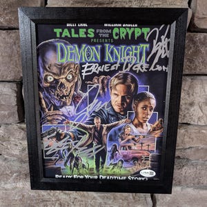 May include: Framed movie poster for "Tales from the Crypt Presents: Demon Knight." The poster features a skull-like figure, actors, and the text "Ready for your deadtime story?" in a black frame. The poster is signed.