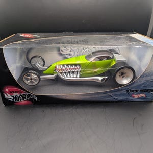 Op de afbeelding: Een limoengroene Hot Wheels gegoten auto in een doorzichtige displaydoos. De auto heeft een strak design met chromen accenten en grote wielen. De doos is voorzien van het Hot Wheels logo en de tekst "Slightly Modified".