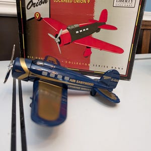 May include: A blue and gold die-cast Lockheed Orion 9 airplane model with the words "Air Eastwood Charter Service" and "E-04" on the side. The model is in its original box, which features a red and black illustration of the plane and the text "Lockheed Orion 9".