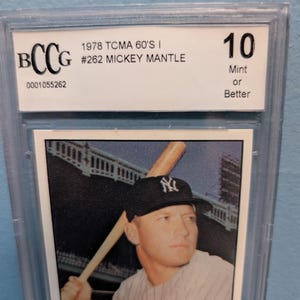 May include: A graded baseball card featuring Mickey Mantle. The card is encased in a protective holder and is graded a 10, labeled "Mint or Better." The card is from the 1978 TCMA 60's I series, card #262.