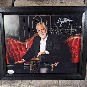 May include: A black framed photo of a man with a beard and mustache sitting on a red velvet couch. He is wearing a black suit and a white shirt. The photo is signed "Jeffery" in the top right corner.