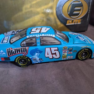 Op de afbeelding: Een turquoise modelraceauto met het nummer 45 op de zijkant en het dak. De auto heeft sponsorlogo's, de naam "Brawny" en een afbeelding van een man met een cowboyhoed. De auto heeft zwarte wielen en het Goodyear-logo.