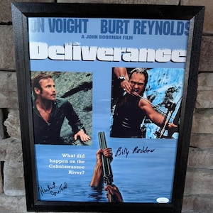 May include: Framed movie poster for "Deliverance" with Jon Voight and Burt Reynolds. The poster features images of the actors and the film's title. Includes the text "What did happen on the Cahulawassee River?" and signatures.