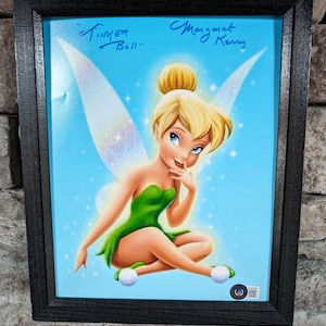 May include: A framed print of Tinker Bell, a fairy with green wings and a green dress, sitting on a blue background. The print is signed "Tinker Bell" and "Margaret Kerry".