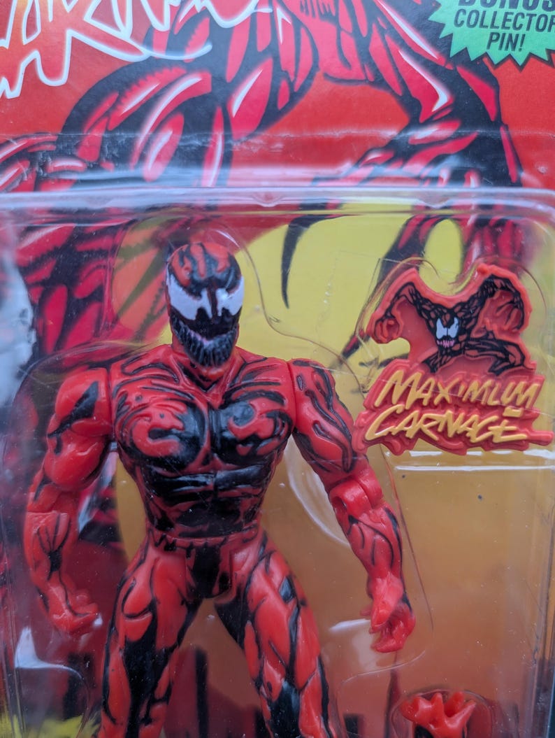 May include: A red and black action figure of the character Carnage from the Marvel Comics series. The figure is in a plastic package with the words "Maximum Carnage" and a bonus collector pin.