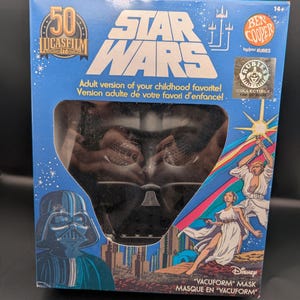 Puede incluir: Una caja azul de Star Wars con una máscara de Darth Vader. La caja presenta el logotipo de Star Wars, el logotipo de Lucasfilm Ltd. y el texto "¡Versión para adultos de tu favorito de la infancia!" La caja también tiene ilustraciones de personajes de Star Wars.