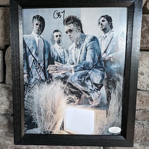 May include: A framed black and white photograph of four men in suits. The men are standing in a field of tall grass. The photograph is signed by all four men. The signature includes the text "G&T".