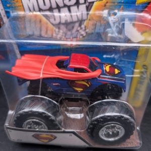 May include: A blue and red Monster Jam truck toy featuring the Superman logo. The truck has large black tires and a red cape. The packaging includes the words "Monster Jam" and "Off Road".
