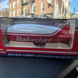 May include: A limited edition Budweiser die-cast metal bank in a box. The airship is white with red stripes and the Budweiser logo. The box is red with the Budweiser logo and text.