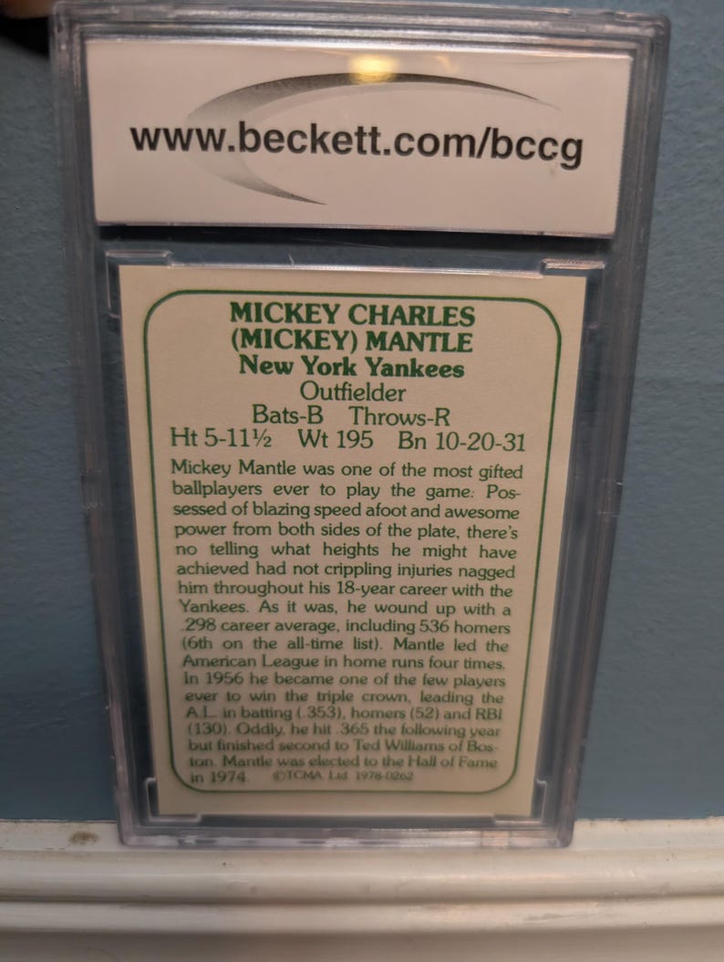 May include: A baseball card encased in a protective holder. The card features Mickey Mantle of the New York Yankees, an outfielder. The card includes his height of 5'11.5", weight of 195 lbs, and birthdate. The Beckett website is visible.