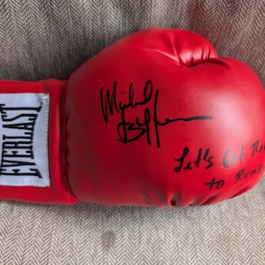 Puede incluir: Guante de boxeo rojo con la marca Everlast blanca. El guante está firmado por Mike Tyson con el mensaje "Let's Get Ready to Rumble".