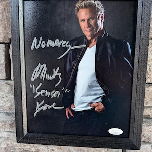 May include: A black framed photo of a man wearing a black leather jacket and a white t-shirt. The man is smiling and looking at the camera. The photo is signed "No mercy,  Munky, 'Sensei' Kane".