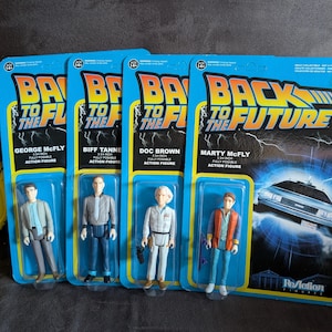 Könnte beinhalten: Vier Back to the Future-Actionfiguren in ihrer Originalverpackung. Die Figuren umfassen George McFly, Biff Tanne, Doc Brown und Marty McFly. Jede Figur ist etwa 9,5 cm groß und wird auf einer blau-gelben Karte mit dem Logo des Films geliefert.