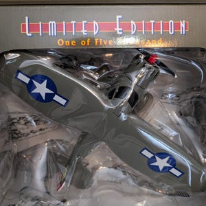 May include: A limited edition, gray, die-cast model airplane with a red propeller and American star decals. The box reads "Limited Edition, One of Five Thousand".