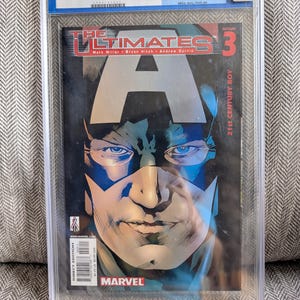 Könnte beinhalten: Ein benotetes Comic-Heft, The Ultimates #3, in einem durchsichtigen Plastik-Etui. Das Cover zeigt eine Nahaufnahme von Captain Americas Gesicht, mit dem Text "The Ultimates" und "Issue 3" in großen, fetten Buchstaben.