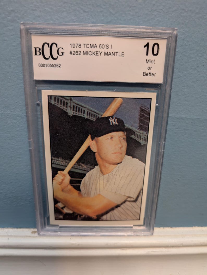 May include: A graded baseball card featuring Mickey Mantle in a New York Yankees uniform, holding a bat. The card is encased in a protective holder and is graded a 10, labeled "Mint or Better". The card is from 1978.