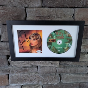 Carátula del CD del álbum The Life Of A Show Girl de Taylor Swift autografiada y enmarcada, con certificado de autenticidad de JSA.