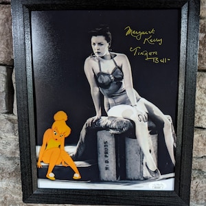May include: A black and white photo of a woman in a swimsuit sitting on a box. The woman is signed "Margaret Kerry Tinkerbell 1934". A cartoon image of Tinkerbell is in the lower left corner of the photo.