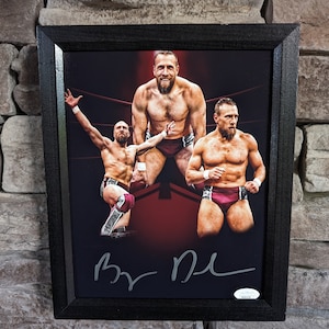 Könnte beinhalten: Ein gerahmtes Schwarzweißfoto von drei Wrestlern in einem Wrestling-Ring. Die Wrestler tragen Wrestling-Hosen und sind in verschiedenen Posen. Das Foto ist unten rechts mit "By The" signiert.