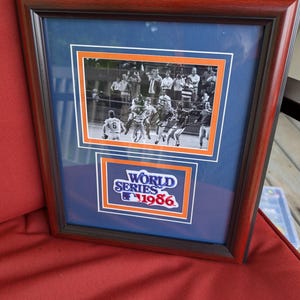 May include: Framed photograph of a baseball game, featuring players in action. The frame is dark brown with a blue matting. The image includes the text "World Series 1986" in a logo.