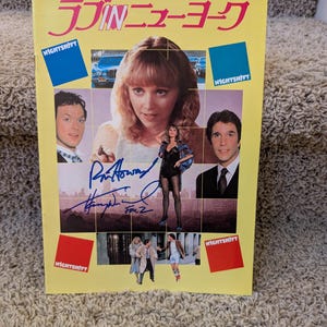 Könnte beinhalten: Ein gelber Werbeflyer für den Film Nightshift mit dem japanischen Titeltext, mehreren Filmszenenbildern und drei deutlichen Unterschriften in blauer Tinte in der Mitte. Das Layout enthält Porträts der Hauptdarsteller.