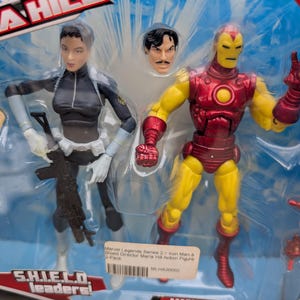 May include: A plastic package containing two action figures, one of Iron Man in a red and yellow suit and the other of Maria Hill in a black and white suit. The package is labeled "Marvel Legends Series 2" and "Iron Man & Shield Director Maria Hill Action Figure 2-Pack".