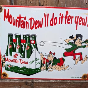 Puede incluir: Un letrero publicitario vintage de Mountain Dew con un personaje de dibujos animados sosteniendo una botella de Mountain Dew. El letrero presenta el texto "Mountain Dew I'll do it fer yew!" y un paquete de seis botellas de Mountain Dew.