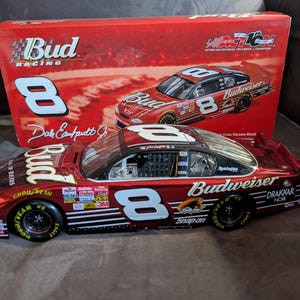 Op de afbeelding: Een rood-zwarte gegoten model raceauto met het nummer 8 en Budweiser-logo's. De auto staat voor een bijpassende doos met het Bud Racing-logo en een foto van de auto. De auto heeft Goodyear-banden.