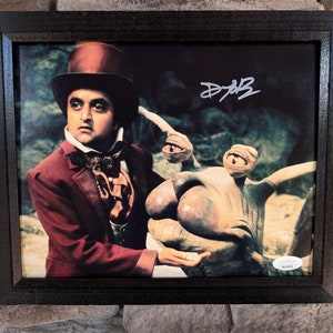 May include: A framed photograph of a man in a top hat and a red jacket, holding a hand out to a three-eyed creature. The man is signing his name "D.A.B." in the top right corner of the photo.