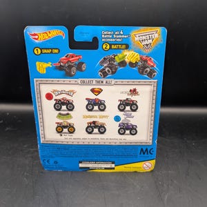 May include: A blue Hot Wheels Monster Jam toy package. The package features images of monster trucks, including "Destroyer" and "Monster Mutt." Text includes "Snap On!" and "Battle!" with the Monster Jam logo.