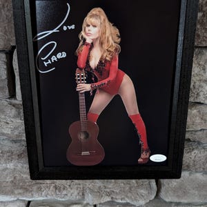 May include: A framed photo of a woman in a red bodysuit holding a guitar. The photo is signed "Love Hard".