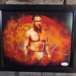 Könnte beinhalten: Ein gerahmter Druck eines Wrestlers vor einem roten und orangefarbenen Hintergrund mit einem Drachenmotiv. Der Wrestler trägt ein weißes Wrestling-Outfit und hat einen Bart. Der Druck ist mit dem Namen des Wrestlers signiert.