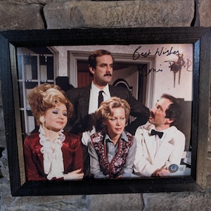 以下が含まれることがあります： ヴィンテージな雰囲気のフレームに入った写真。4人の人物が写っており、おそらく俳優と思われる。写真には「Best Wishes」のサインと文字が書かれている。被写体は時代衣装を身につけており、男性はスーツとネクタイ、その他はフォーマルな服装をしている。