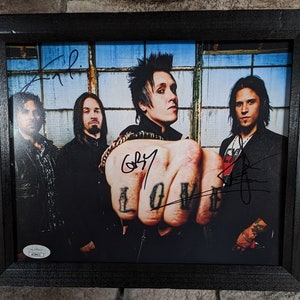 May include: A framed black and white photograph of a band with four members. The band members are all wearing black clothing. The photograph is signed by all four band members. The photograph is framed in a black frame with a white mount.