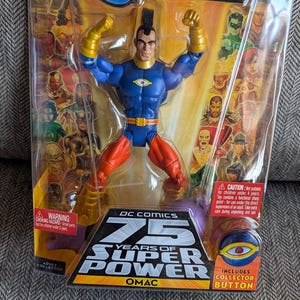 May include: DC Universe Classics OMAC action figure in a plastic package. The figure is blue and red with a yellow belt and a single eye on his chest. The package includes a collector button. The package has the text "DC Comics 75 Years of Super Power OMAC" on it.
