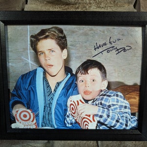 May include: A framed photograph of two young boys watching television. The boys are holding boxes of popcorn. The photo is signed "Have fun...  Tony Dow".